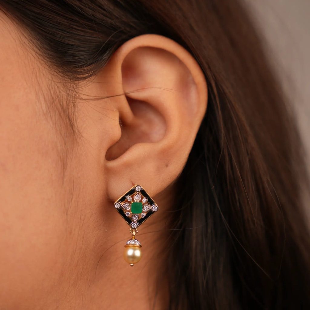 Close-up of a decorative earring with gemstones and pearl drop on a woman’s ear.