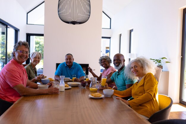 Group of older adults enjoying a shared meal around a dining table in a bright modern home, smiling and socializing together.